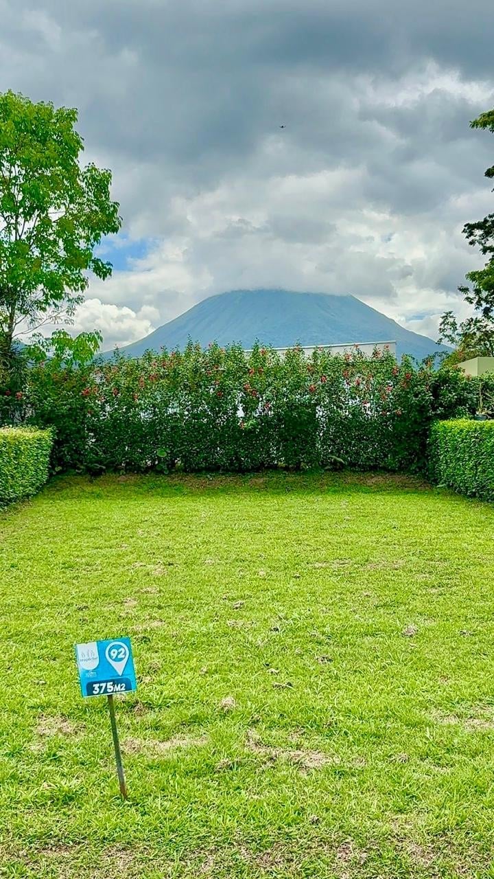 Green lawn with blue property marker sign facing a distant mountain and hedges under cloudy sky